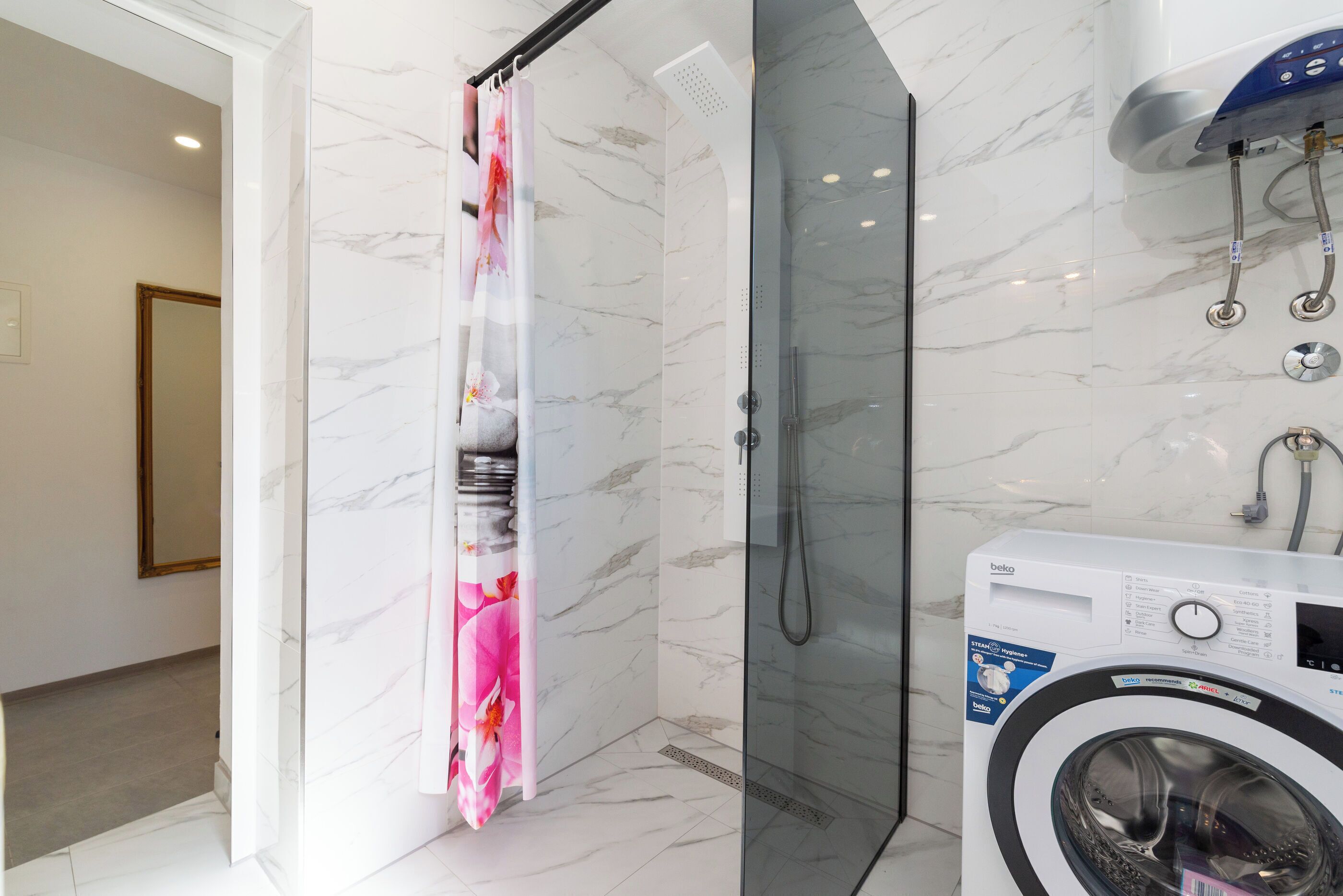 A bathroom with a glass-enclosed shower, a washing machine, and a marble-tiled wall.