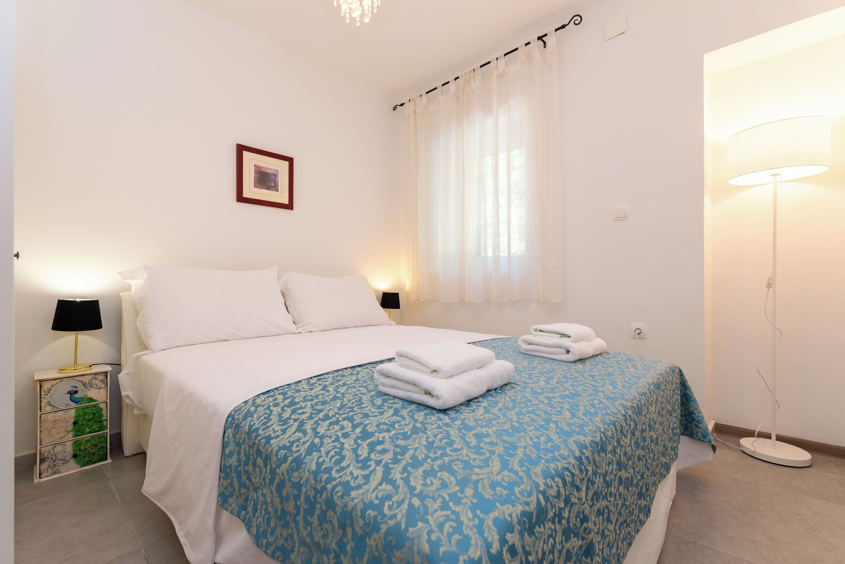 A neatly made bed with white linens, a blue patterned bedspread, and two folded towels on the bed.