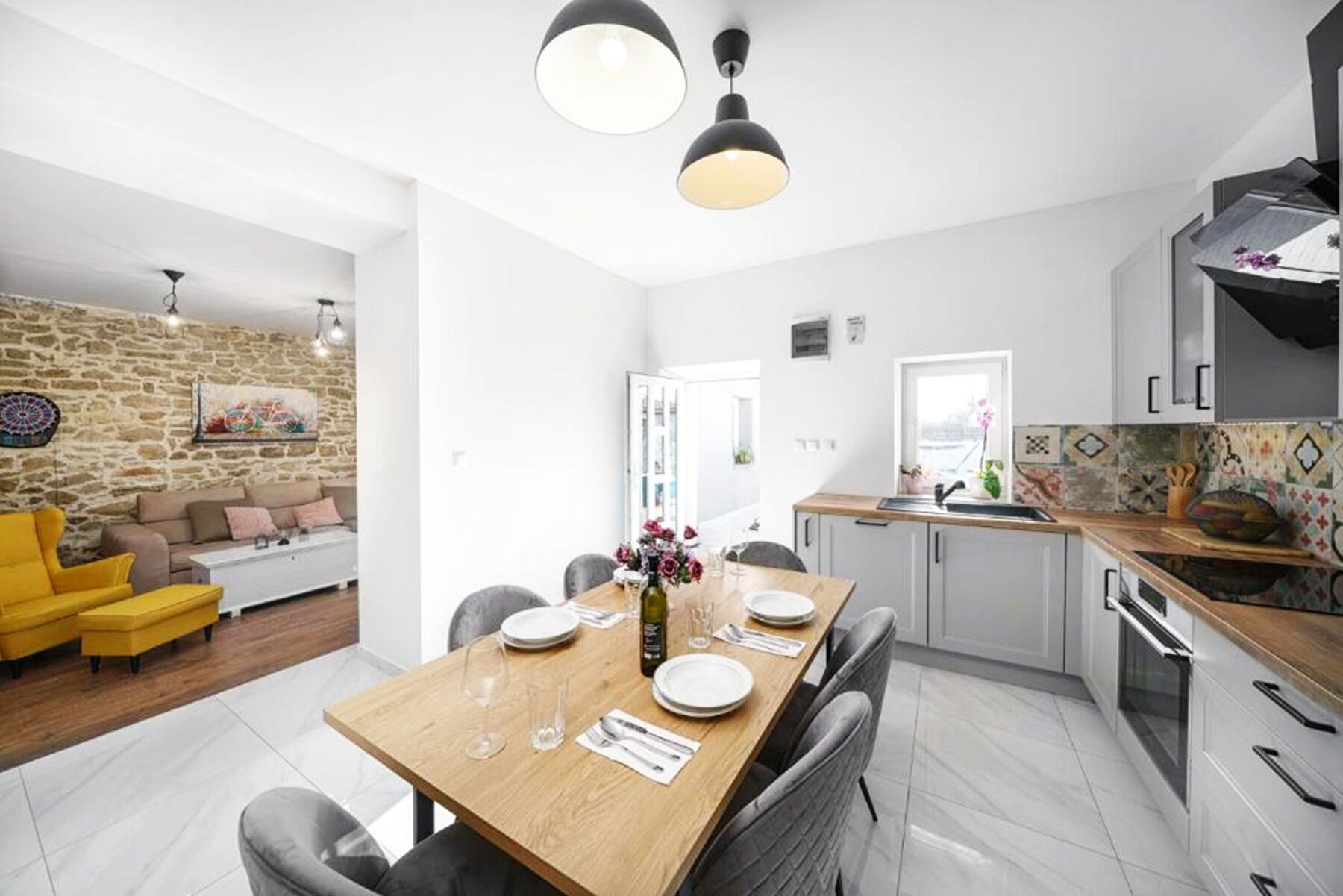 A modern kitchen with a dining area, stone wall, and a yellow armchair.
