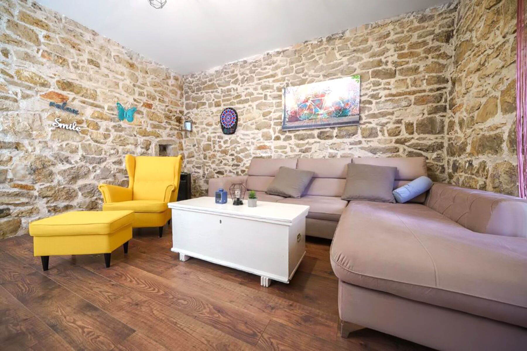 Ein Zimmer mit Steinwänden, einem gelben Sessel, einem weißen Couchtisch, einem beigen Sofa und einem Gemälde.
