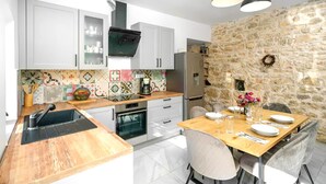 A modern kitchen with white cabinets, a stone wall, and a dining area with a wooden table and chairs. - Villa Dalmatian Dream (Benkovac)