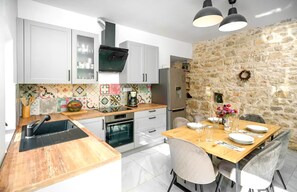 Eine moderne Küche mit weißen Schränken, einer Steinwand und einem Essbereich mit Holztisch und -stühlen.