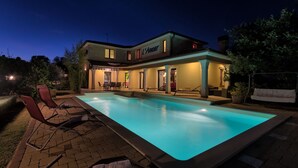 Una casa moderna con piscina, area relax esterna e facciata ben illuminata.