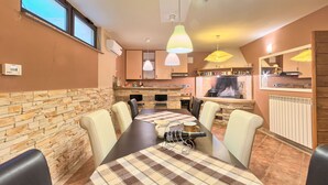 Zona pranzo con tavolo, sedie, camino e cucina sullo sfondo.
