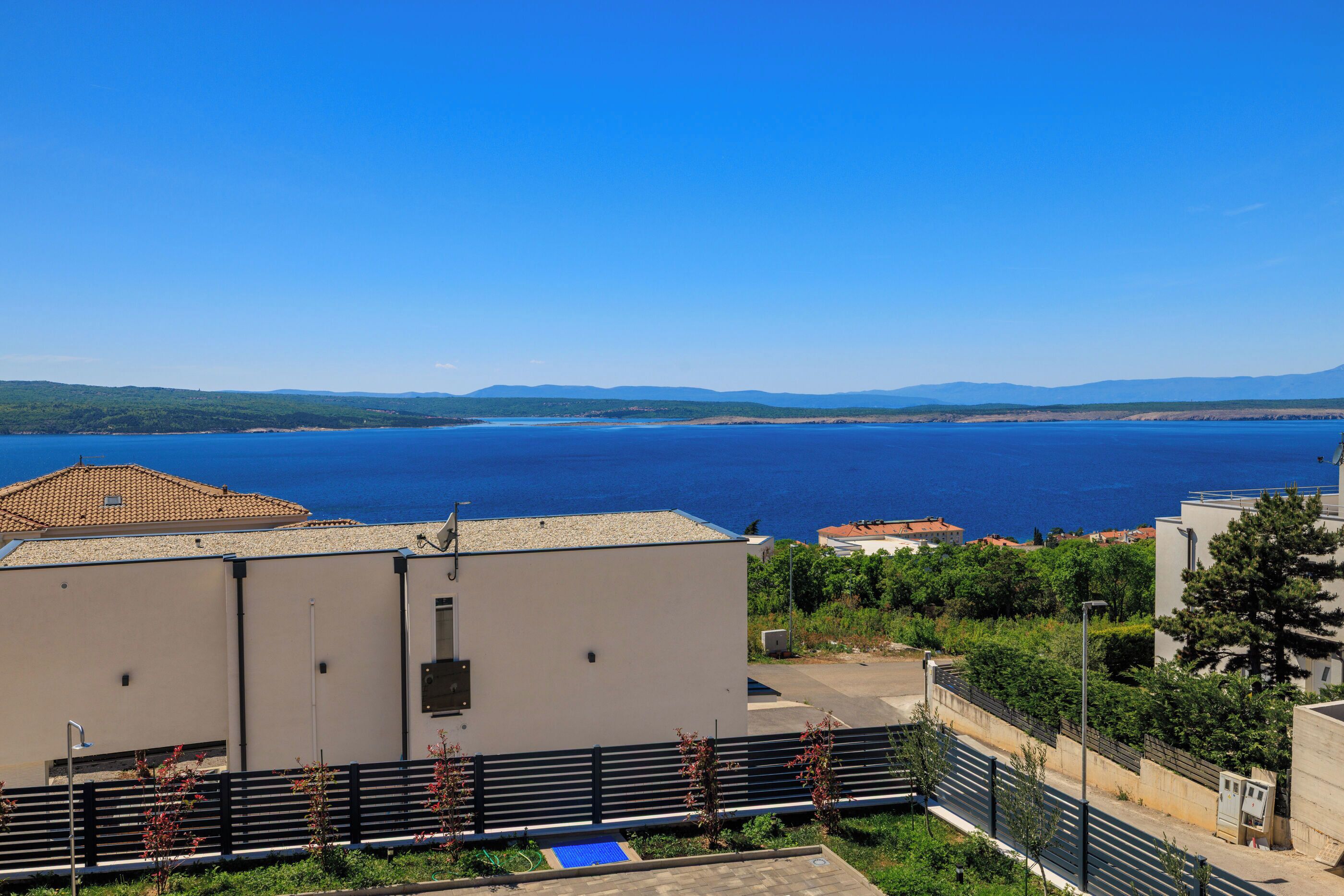 A coastal building with a view of the sea, a paved area with a blue mat, and a fence.