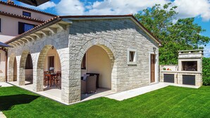 A stone building with arched doorways, a patio with outdoor furniture, and a barbecue area. - Villa Casa Mia (Barban)