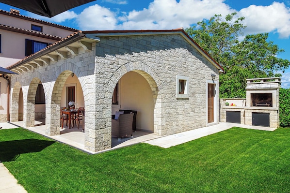 A stone building with arched doorways, a patio with outdoor furniture, and a barbecue area.