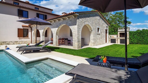 A poolside area with lounge chairs, a table with drinks, and a stone building with arches. - Villa Casa Mia (Barban)