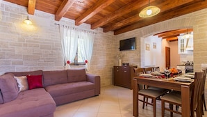 A living room with a sofa, dining table, and chairs, a kitchen area with cabinets and a TV, and a stone wall. - Villa Casa Mia (Barban)