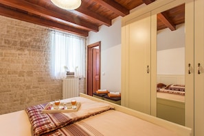 A bedroom with a bed, a tray with drinks, a window with curtains, a radiator, and a wardrobe.