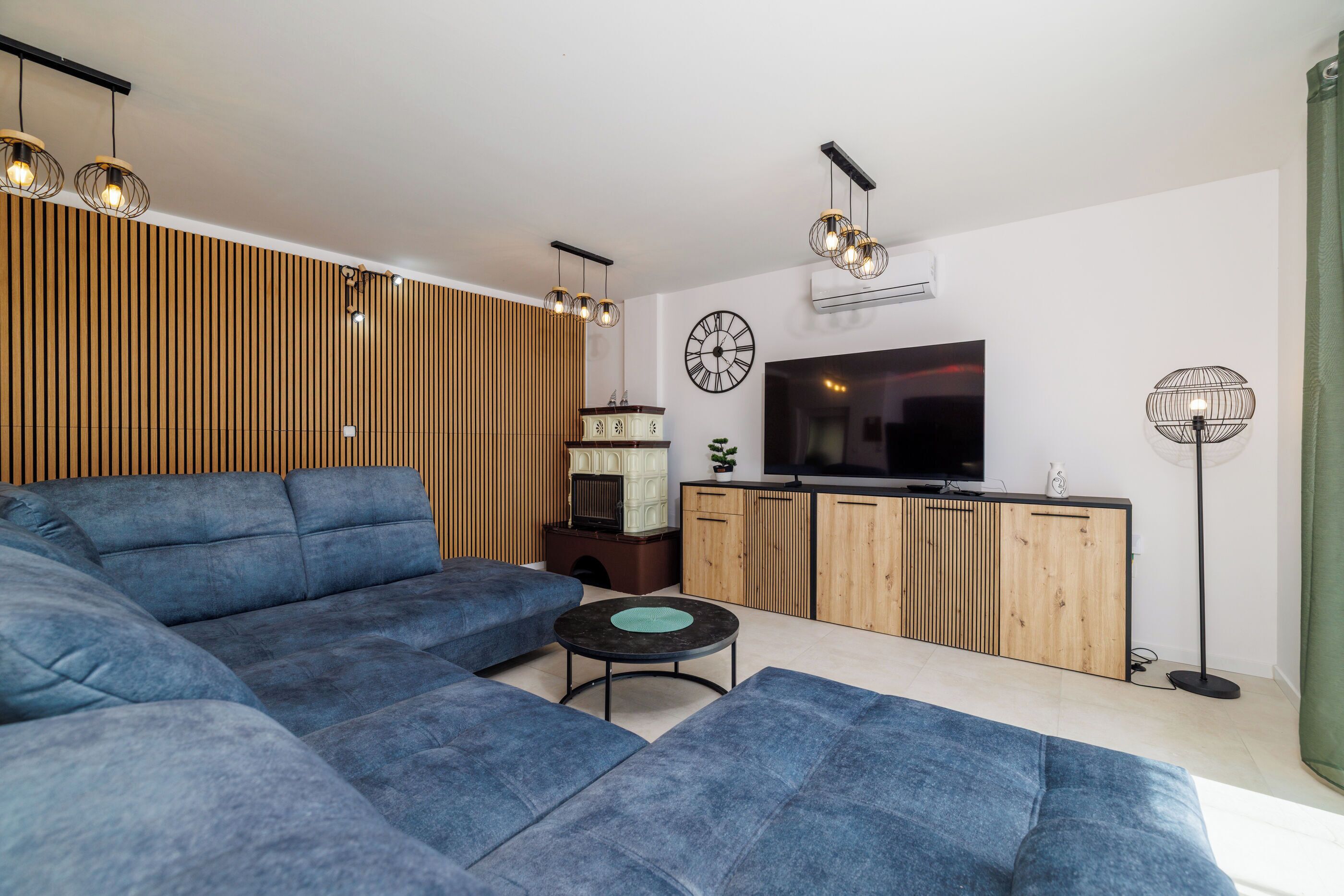 Ein modernes Wohnzimmer mit einer Eckcouch, einem kleinen runden Tisch, einem Fernseher und einer Holzkommode.