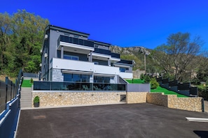 A modern multi-story building with a stone facade, large windows, and a parking area. - Villa Hermosa (Vinodol)
