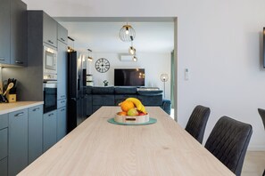 A modern kitchen with grey cabinets, a wooden dining table, and a fruit bowl. - Villa Hermosa (Vinodol)