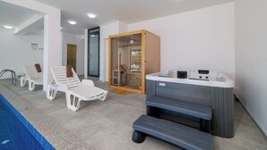 Moderni sisäuima-alue, jossa on aurinkotuoleja, poreallas ja lasiseinällä varustettu sauna.