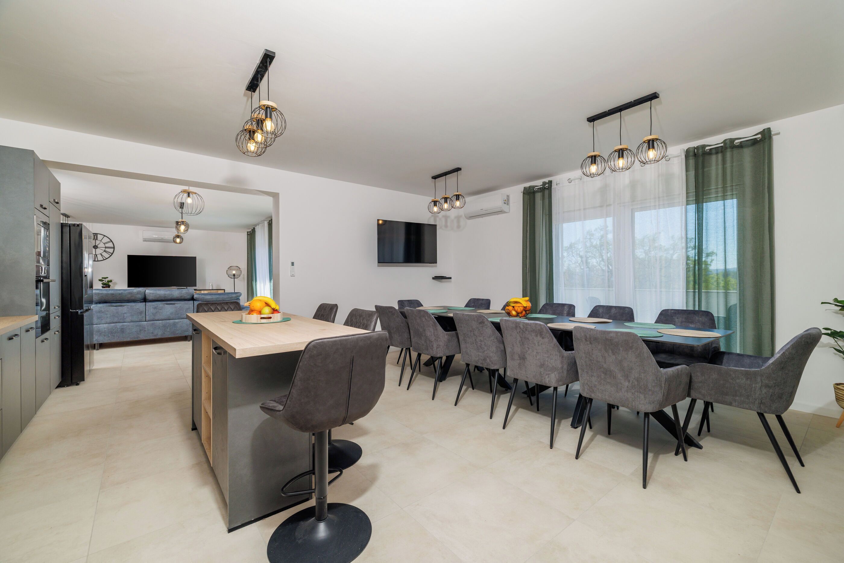 A modern kitchen with a dining area, grey chairs, and pendant lighting.