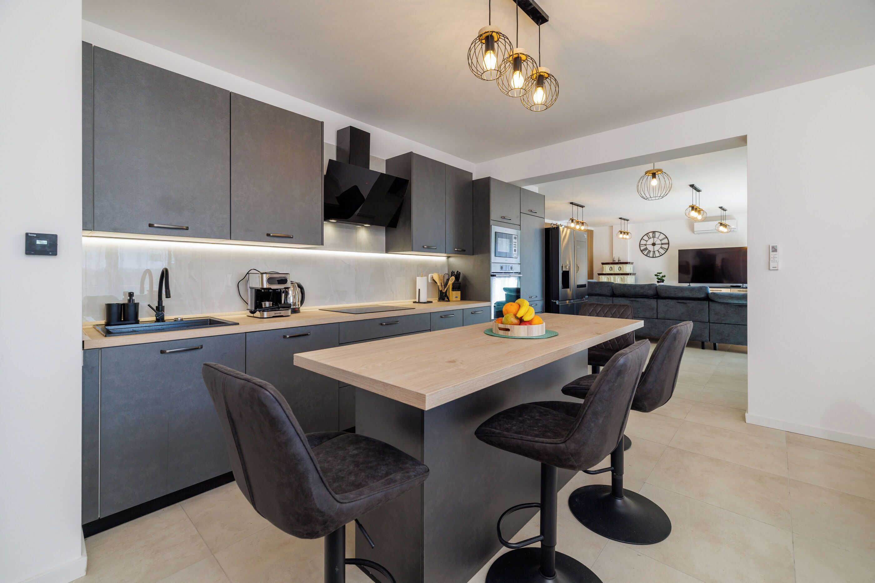 A modern kitchen with grey cabinets, a wooden island, bar stools, and pendant lighting.