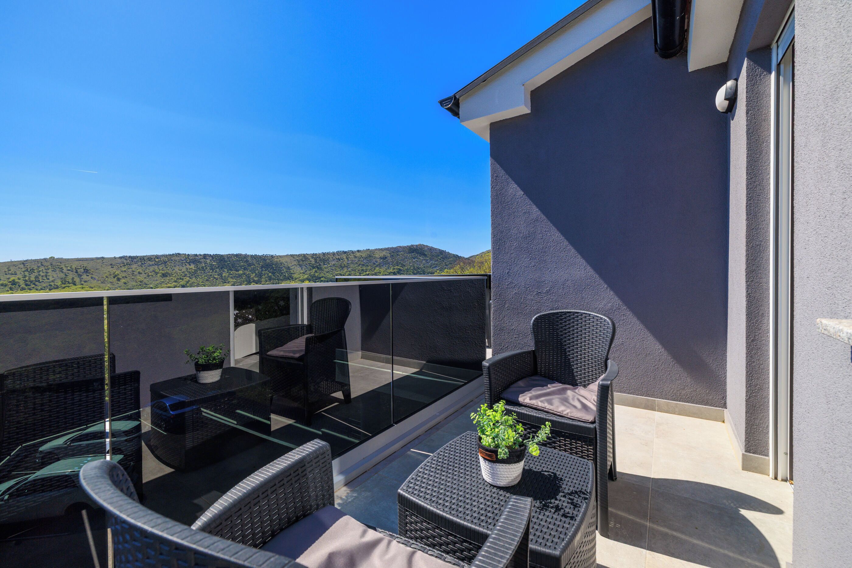 A balcony with wicker furniture, a glass table, and a potted plant.