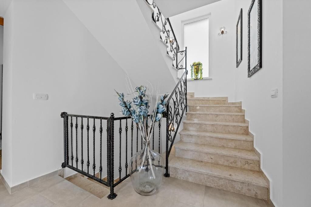 A staircase with a black metal railing, a clear glass vase with flowers, and a window with a plant.