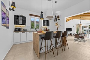 Eine moderne Küche mit einer zentralen Kochinsel, Barhocker, Pendelleuchten und einem Essbereich mit Holzboden.