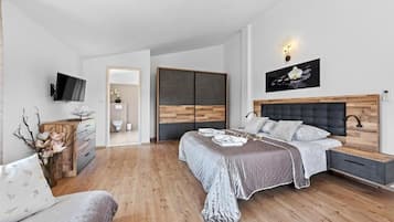 Een moderne slaapkamer met een bed, nachtkastjes, een televisie en een houten garderobe.
