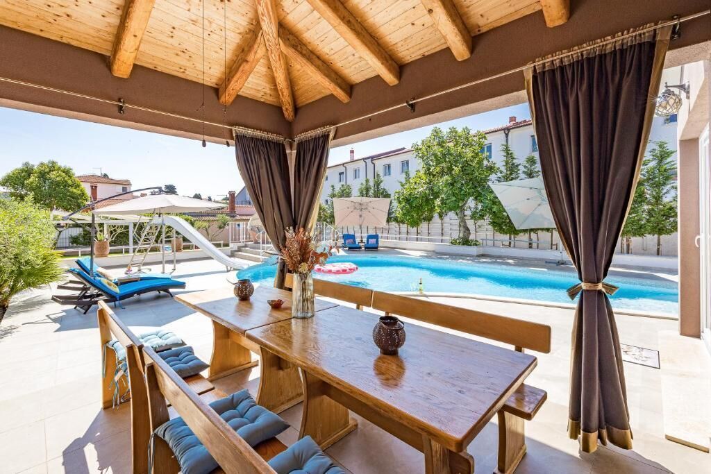 Une terrasse extérieure avec une piscine, des meubles en bois et des rideaux.