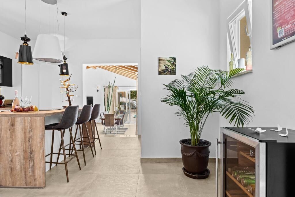 Une cuisine moderne avec un îlot central en bois, des tabourets de bar, des luminaires suspendus et une plante en pot.