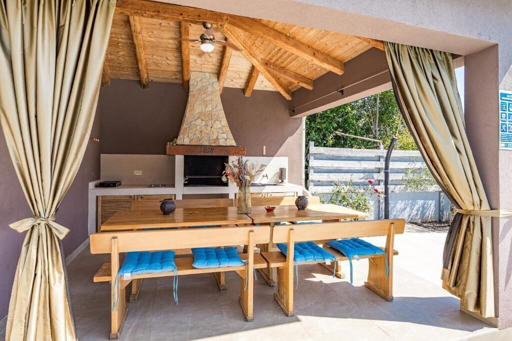 An outdoor dining area with a wooden table and benches, a stone chimney, and a view of the surrounding landscape.
