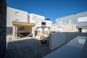 Ein moderner Außenbereich mit Terrasse, einer Sitzecke, einer Feuerstelle und einer Pergola.