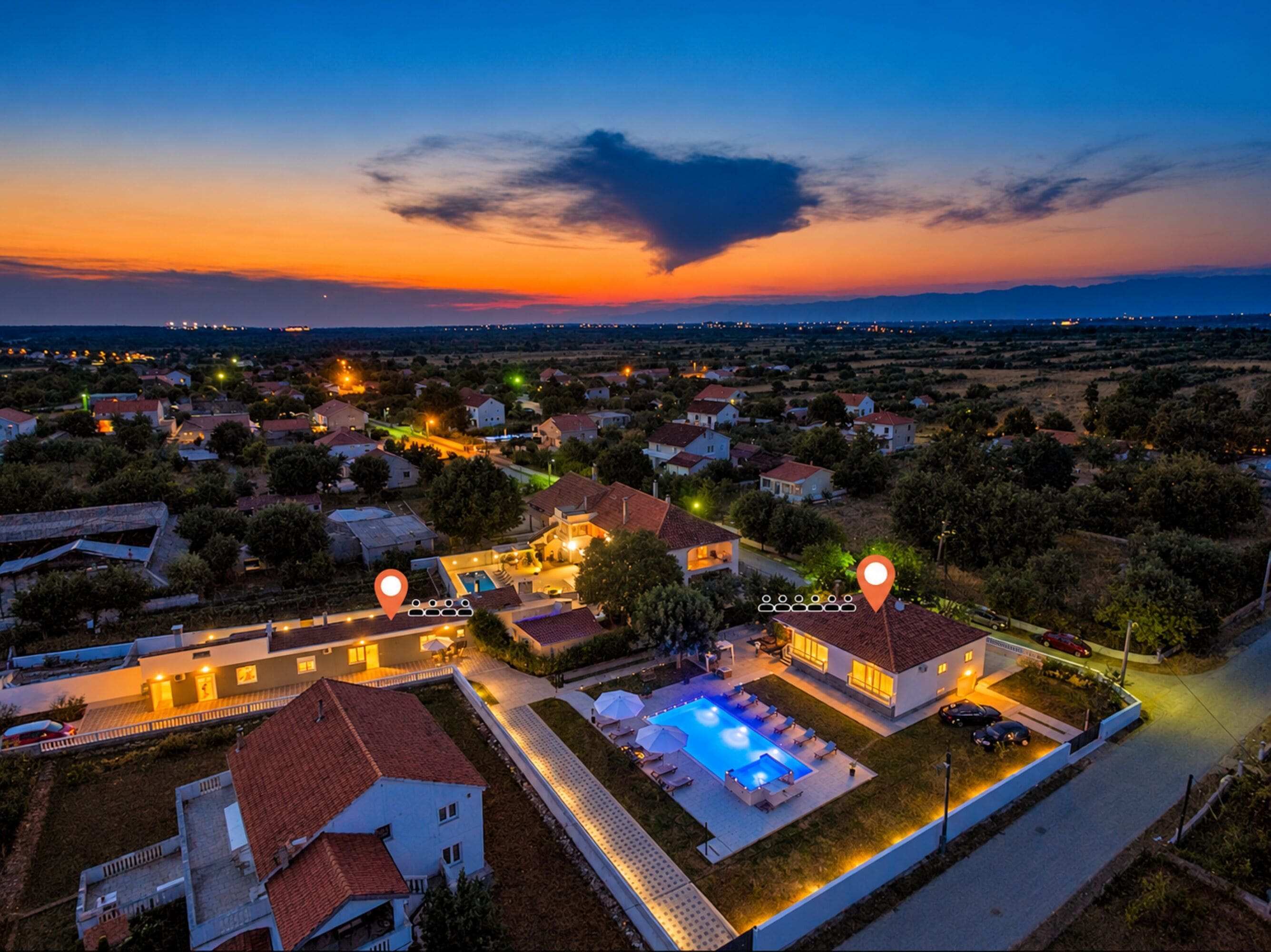 An aerial view of a residential area with houses, a swimming pool, and a sunset.