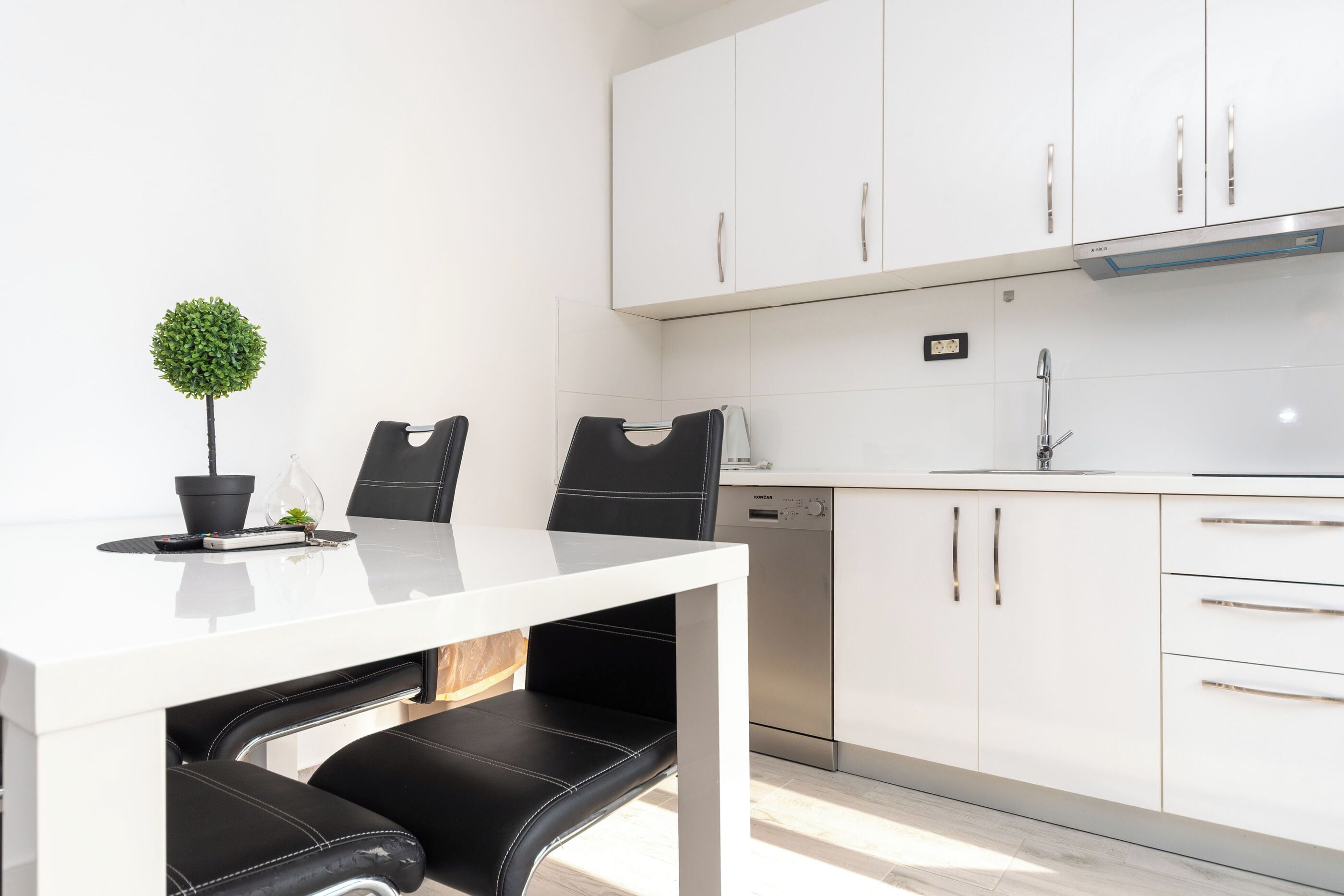 Une cuisine moderne avec des meubles blancs, un lave-vaisselle en acier inoxydable et une table à manger noire accompagnée de deux chaises.