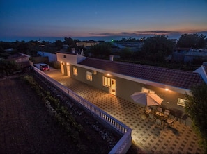 Ein zweistöckiges Haus mit Balkon, ein geparktes Auto davor und eine Terrasse mit Gartenmöbeln.
