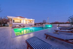 Ein modernes Haus mit Swimmingpool, Liegestühlen und einer gut beleuchteten Fassade.