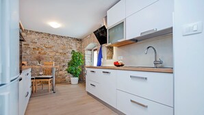 A modern kitchen with white cabinets, a stone wall, a wooden dining table, and a potted plant. - Villa Masi (Kanfanar)