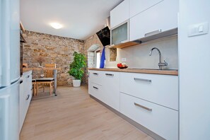A modern kitchen with white cabinets, a stone wall, a wooden dining table, and a potted plant. - Villa Masi (Kanfanar)