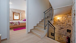 A bedroom with a stone wall, a wooden bed, and a staircase with a metal railing. - Villa Masi (Kanfanar)