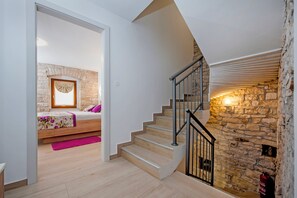 A bedroom with a stone wall, a wooden bed, and a staircase with a metal railing. - Villa Masi (Kanfanar)