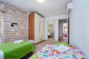 Ein Zimmer mit einer Steinwand, einem Holzschrank, einem Bett mit floralem Überwurf und einer grünen Tagesdecke.