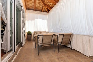 A covered patio area with a table and chairs, a sofa, and a potted plant.