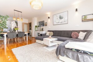 Ein modernes Wohnzimmer mit grauem Sofa, weißem Couchtisch und einem Essbereich mit Holztisch und Stühlen.