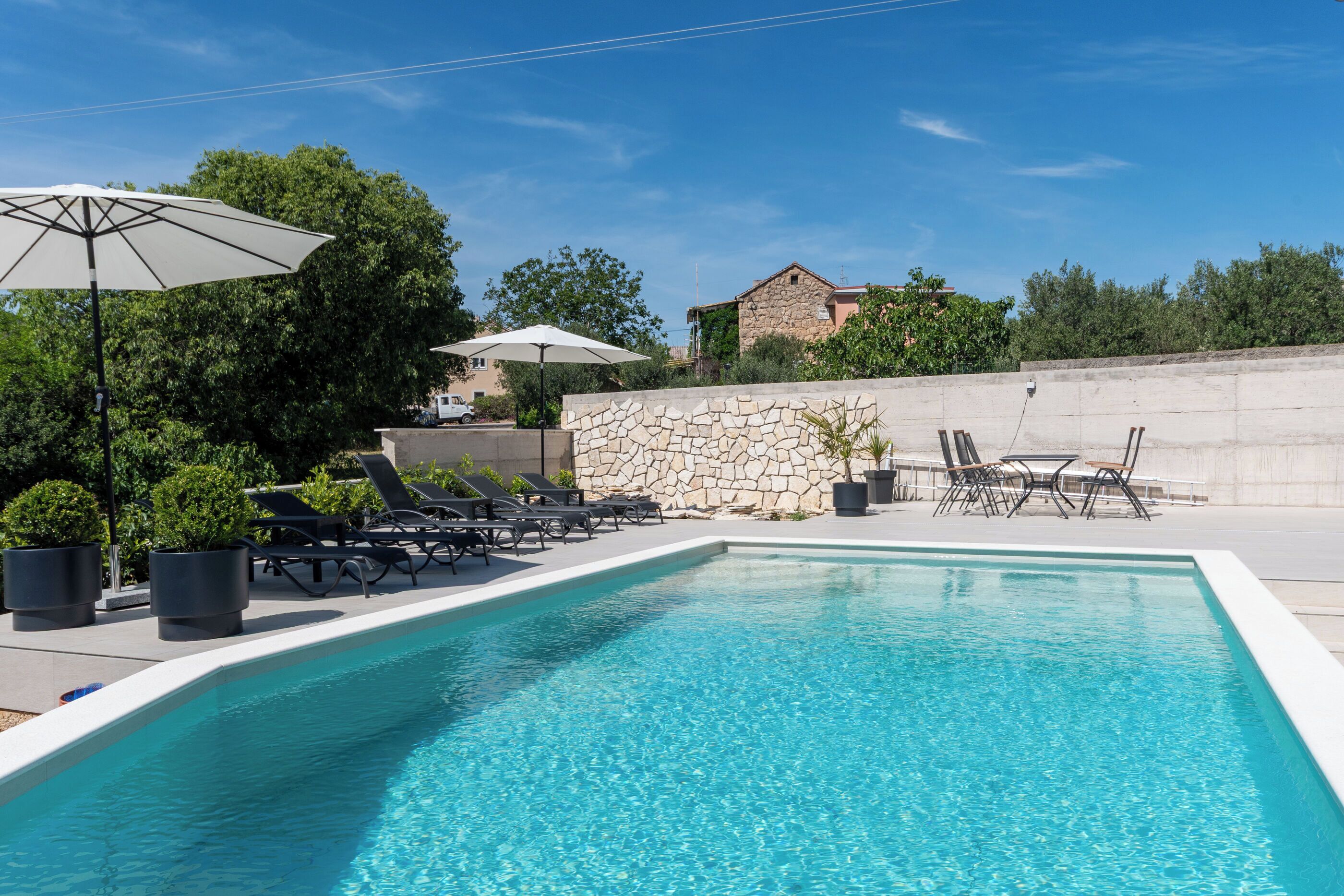 Una piscina con lettini e ombrelloni, circondata da muri in pietra e vegetazione.