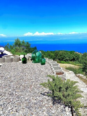 Un paysage rocheux parsemé de bouteilles en verre vert, un objet sphérique et une vue sur la mer et les montagnes lointaines.