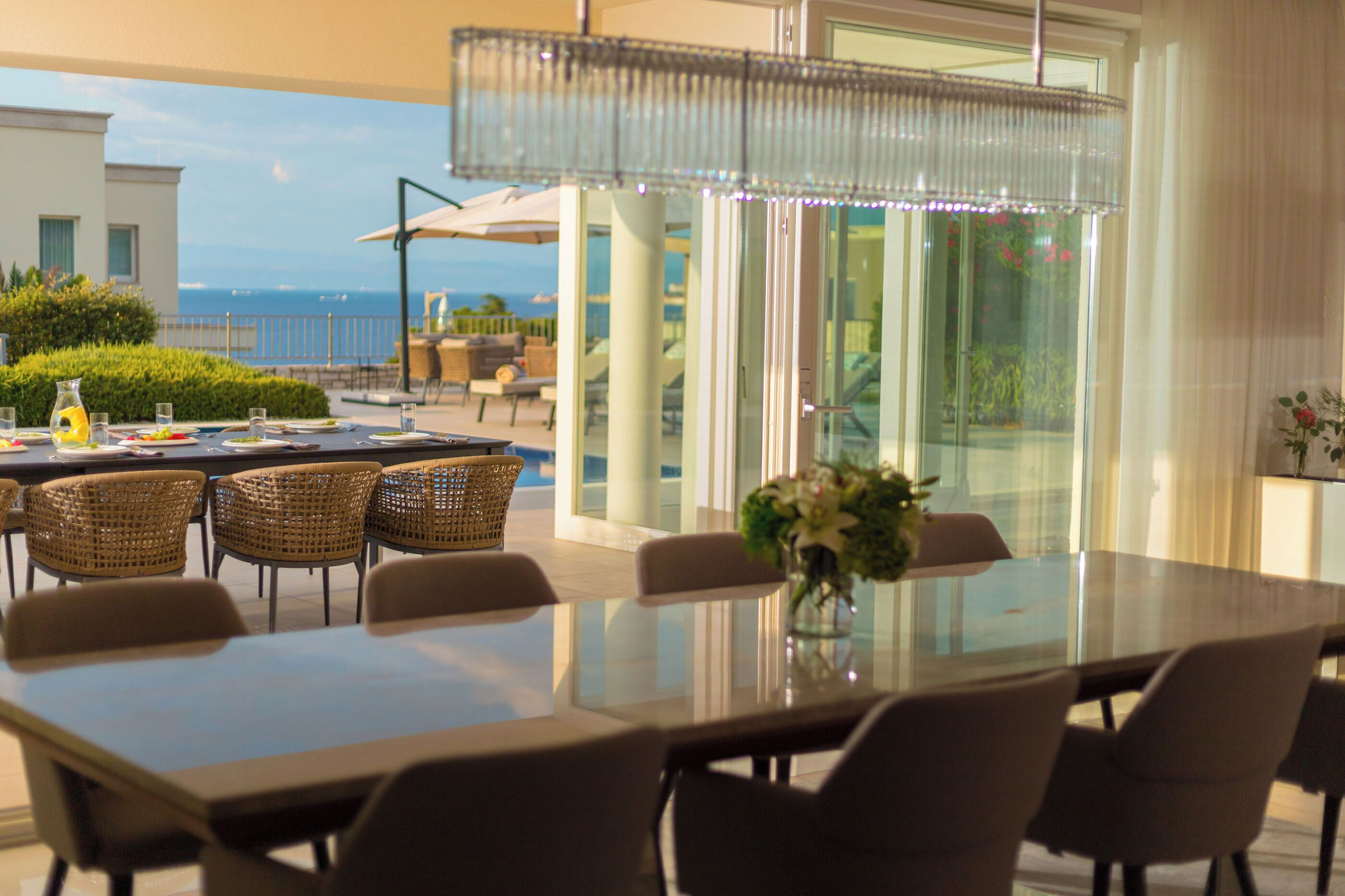 Un coin repas avec une table en verre, des chaises en osier et une vue sur l’océan.