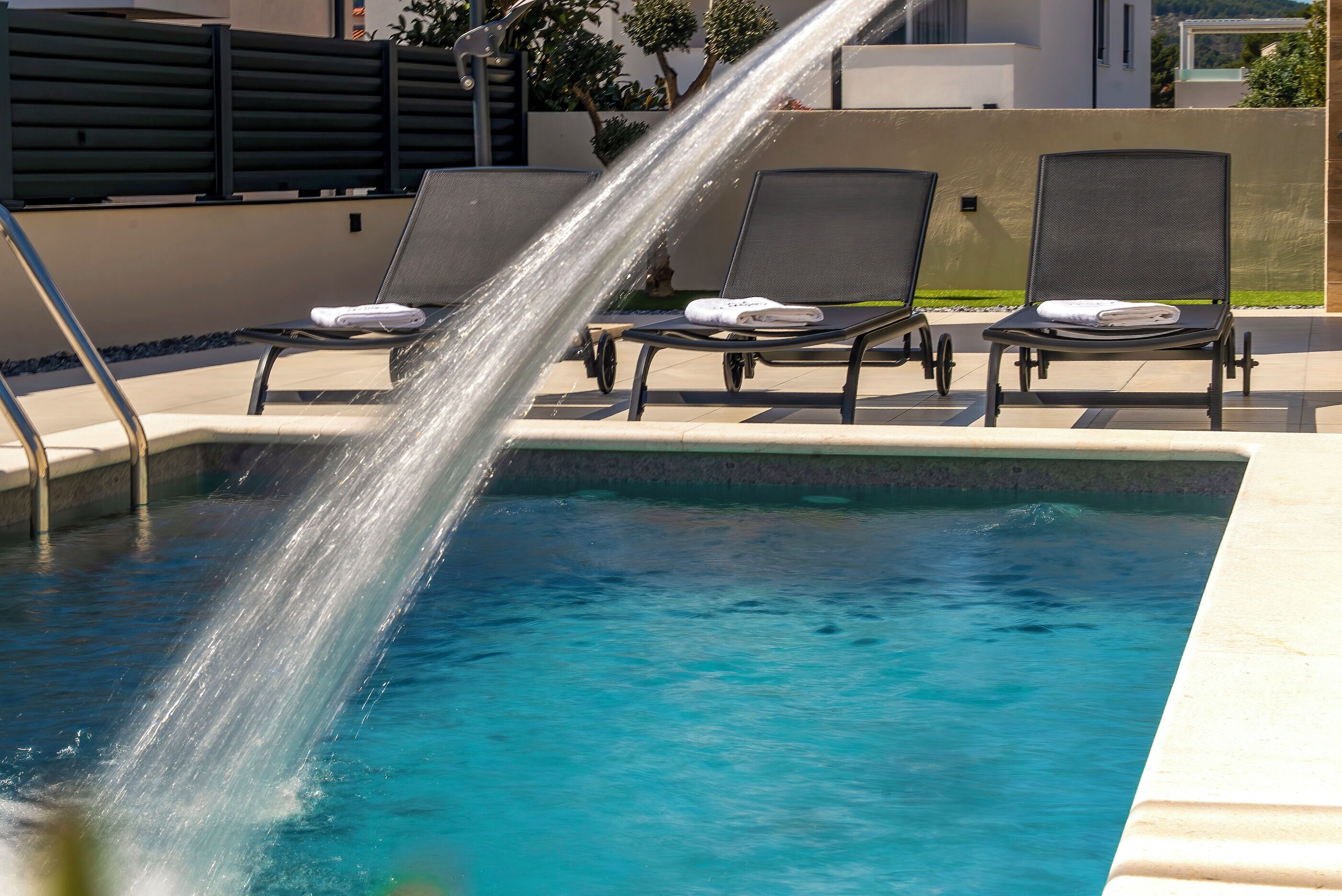 Piscina com toboágua, espreguiçadeiras e um edifício moderno ao fundo.
