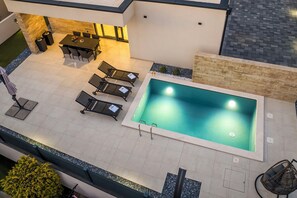 Ein Poolbereich auf dem Dach mit Tisch und Stühlen, einer Liege und einem kleinen Garten.