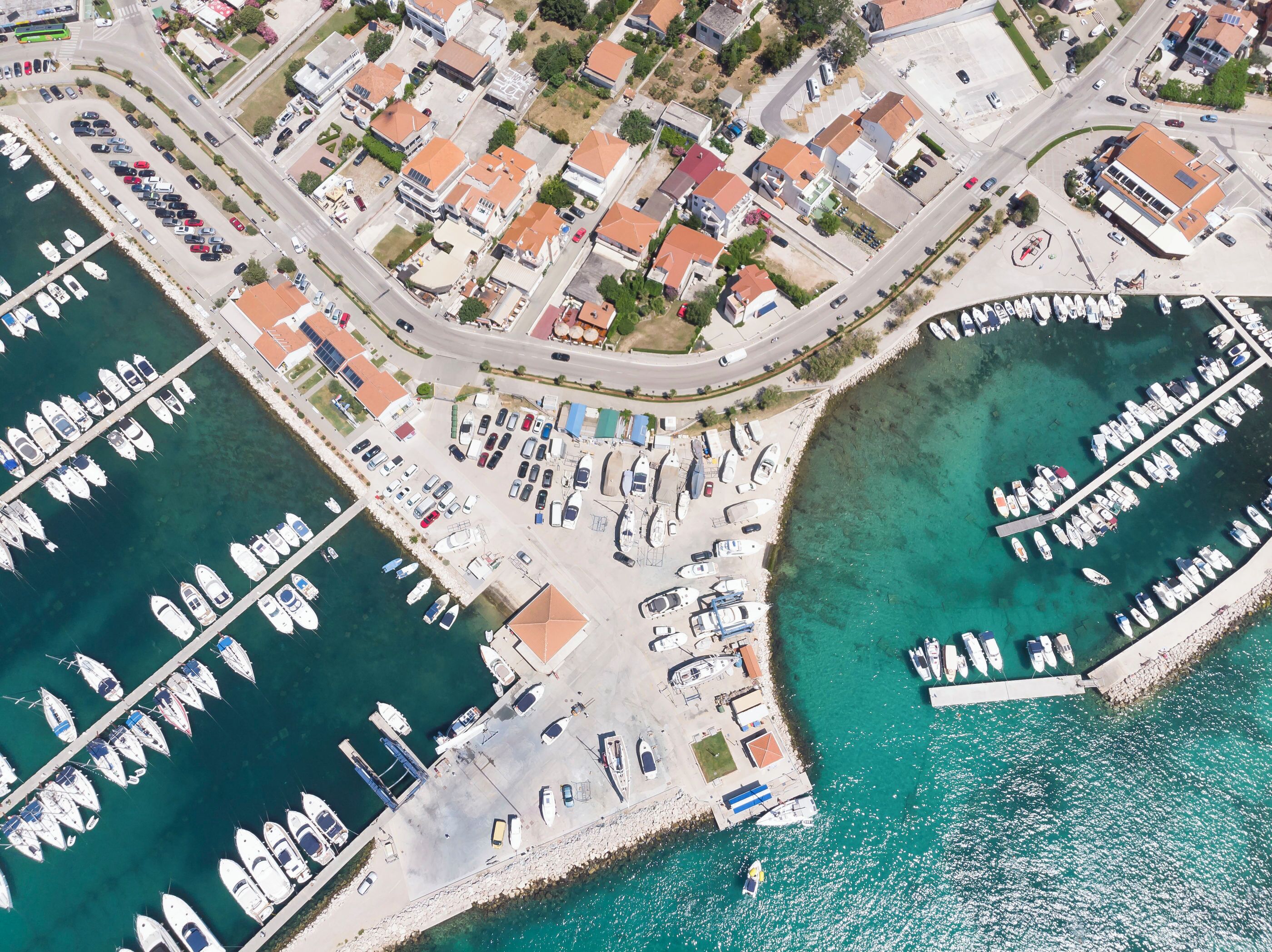 An aerial view of a marina with boats docked, a parking area, and residential buildings.