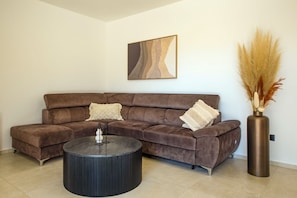 Ein braunes Ecksofa mit zwei Zierkissen, einem runden schwarzen Couchtisch und einer hohen Vase mit Pampasgras.