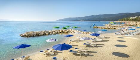 A beach with clear water, lounge chairs, and umbrellas.