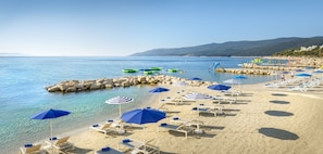 Ein Strand mit klarem Wasser, Liegestühlen und Sonnenschirmen.