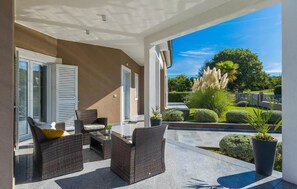 A covered outdoor seating area with wicker furniture, a glass table, and potted plants. - Villa Deep Blue (Labin)