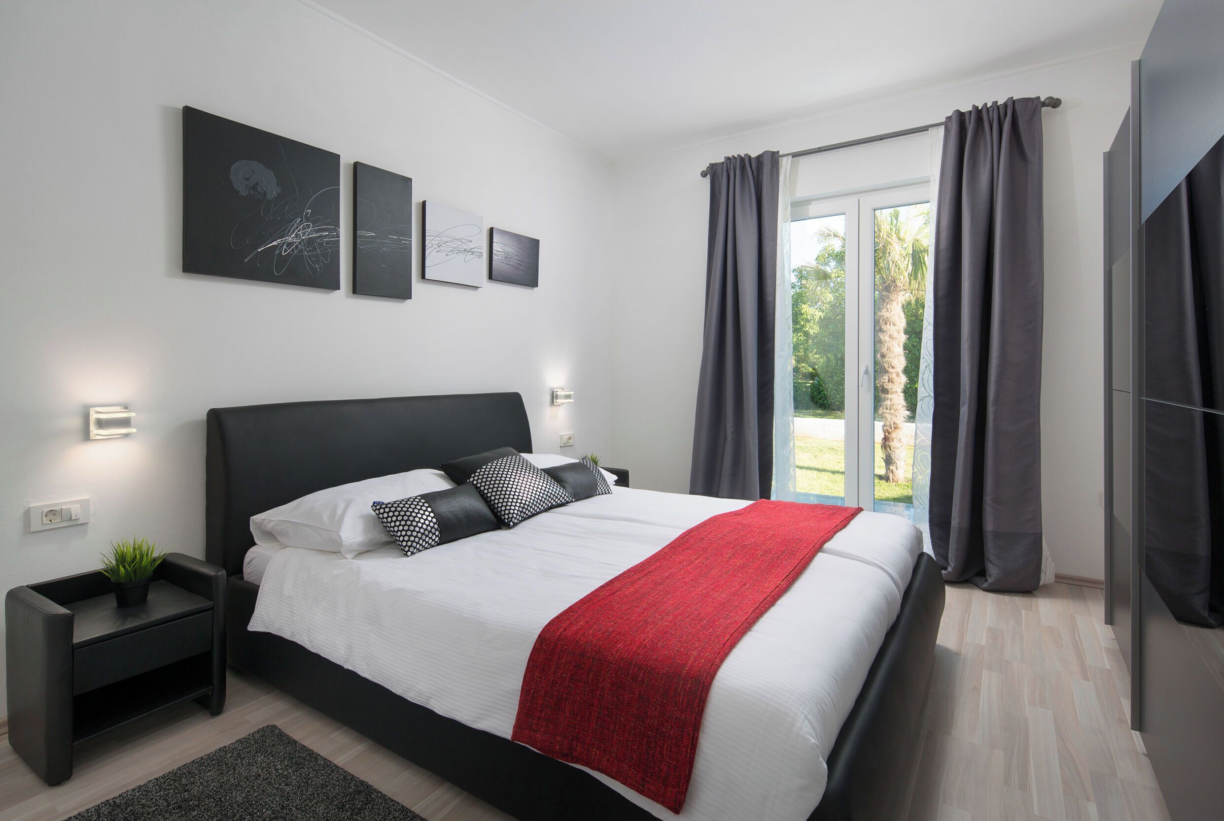 Un dormitorio moderno con una cama grande, una mesita de noche, un plaid rojo y una obra de arte en la pared.